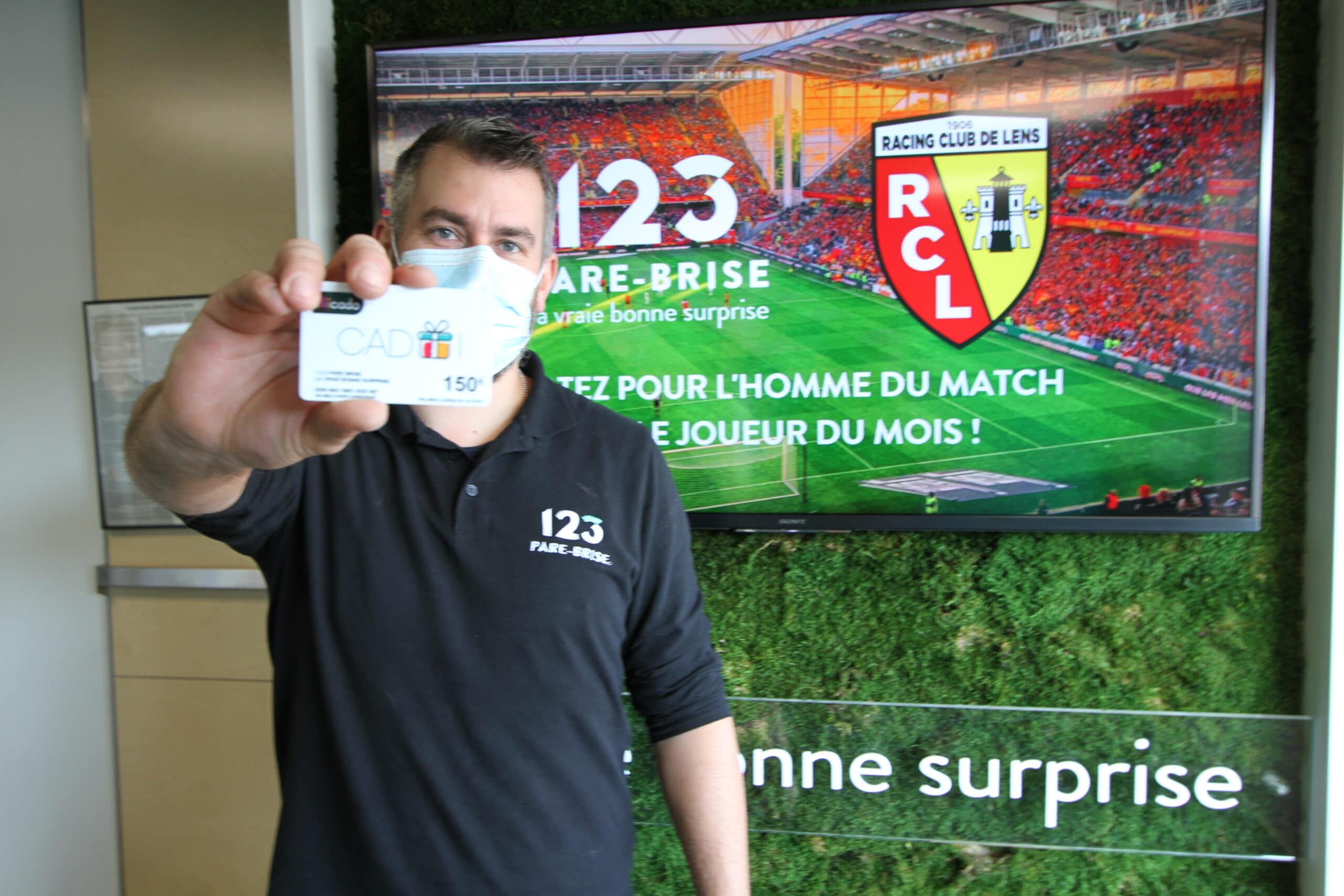 Chef de centre Joffrey qui tient une carte cadeau de 150€ dans sa main devant un écran RC Lens