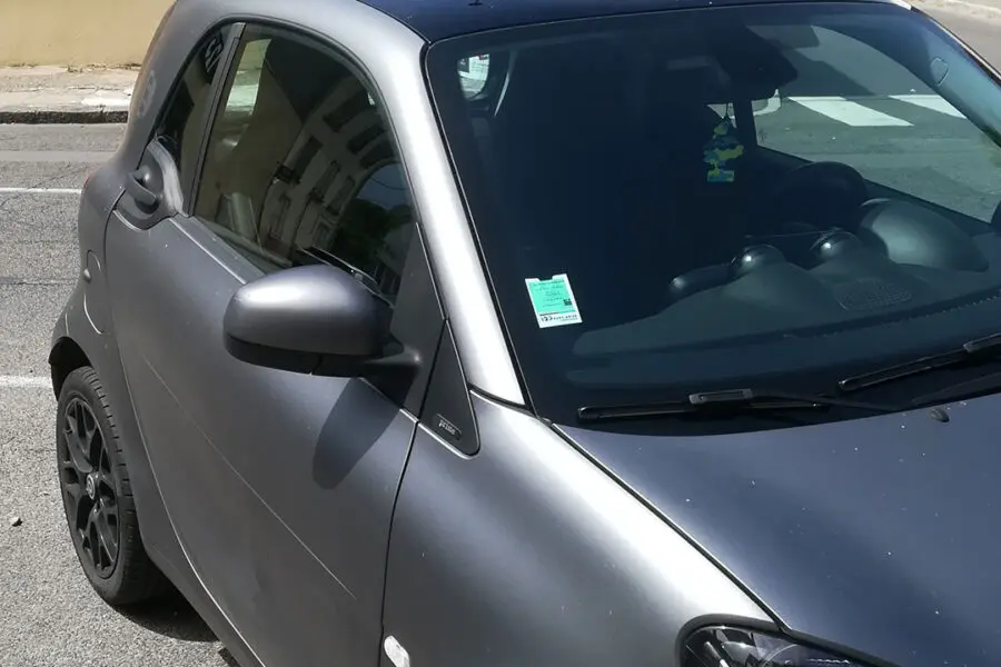 Vignette auto assurance collée sur un pare-brise d'un véhicule garé dans une rue.